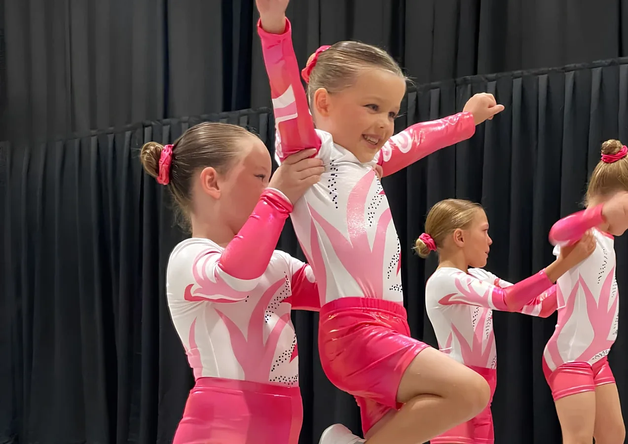 Young cheerleaders in pink and white uniforms performing a lift on stage